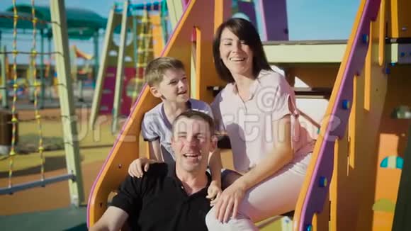 快乐的家庭在夏天一起在操场上度过闲暇时光父亲和儿子坐在楼梯上视频的预览图