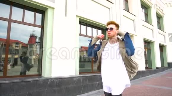 一个穿着时髦衣服的年轻红发男子在城里散步摘下太阳镜的肖像视频的预览图