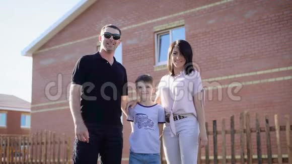 在阳光明媚的夏天一家人穿着休闲服装站在他们的新房子附近父亲母亲和视频的预览图