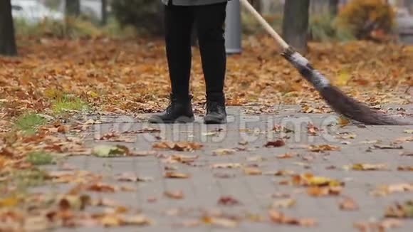 穿着破旧靴子的街道清洁工在秋天公园扫干树叶低工资的工作视频的预览图
