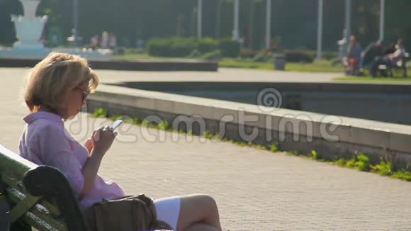 年轻女性坐在公园里在智能手机上聊天在小工具上阅读新闻视频的预览图
