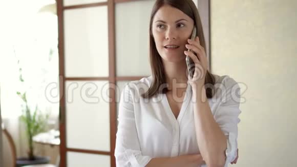 穿着白色衬衫的休闲年轻女子站在客厅里打电话收到坏消息视频的预览图