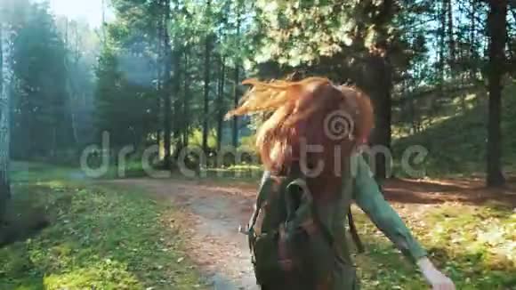 一个年轻漂亮的红发女孩带着背包走在森林或公园里独自旅行时髦的步行者视频的预览图