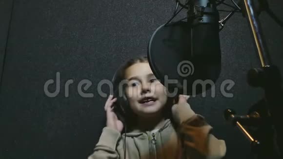 小女孩唱片把一首歌唱到音乐工作室的麦克风里女孩在工作室里唱摇滚歌曲视频的预览图