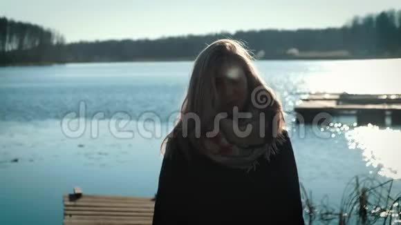 一个身穿外套的金发美女站在湖边的码头上湖面上秋天和多云的心情视频的预览图