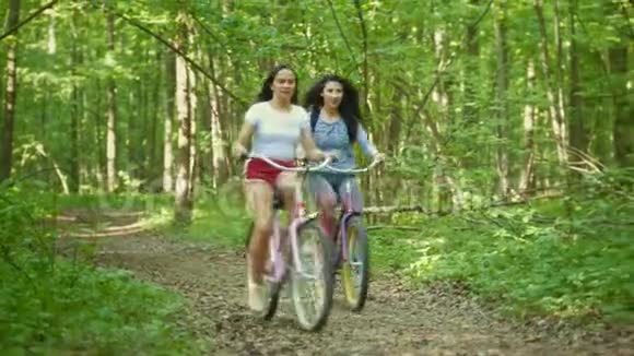 两个女孩骑着自行车在绿色森林里散步夏日视频的预览图