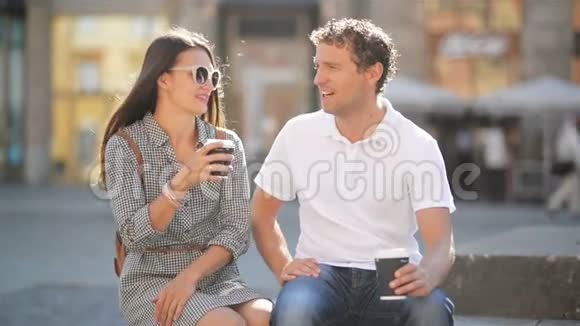 快乐的情侣在阳光明媚的夏日坐在城市广场的长凳上喝咖啡视频的预览图