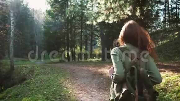 一个年轻漂亮的红发女孩带着背包走在森林或公园里独自旅行时髦的步行者视频的预览图