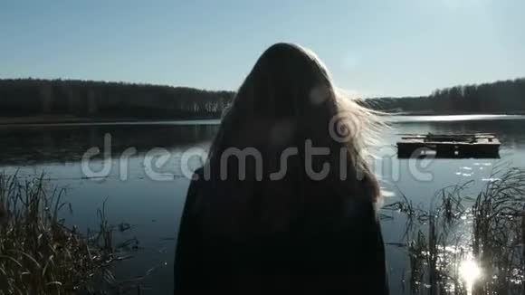 一个穿外套的漂亮金发女孩正走在湖边的码头上在湖面上秋天和多云的心情视频的预览图