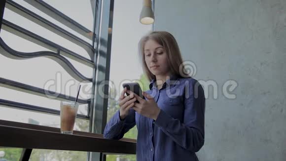 漂亮的女孩坐在窗边在咖啡馆里拿着电话视频的预览图