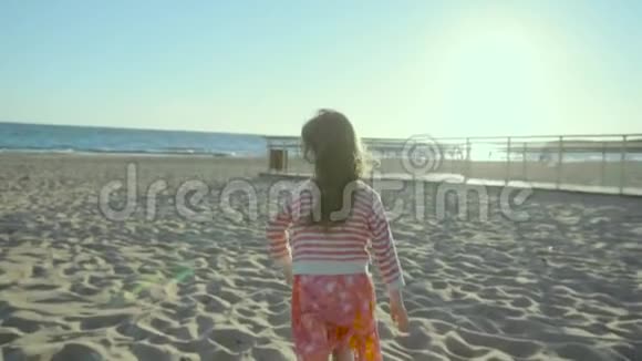 害羞的小女孩跑开停下来在海上的岸边在夕阳下在懒洋洋地转过身视频的预览图