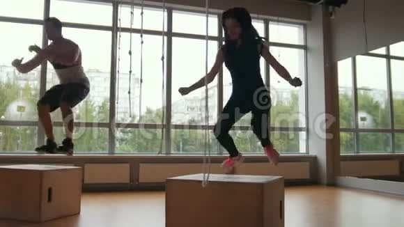 运动的女人和肌肉发达的男人健身教练在健身房锻炼时做盒子跳跃运动视频的预览图