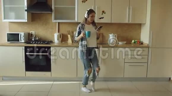 迷人的年轻有趣的女人戴着耳机早上在厨房跳舞唱歌玩得开心视频的预览图