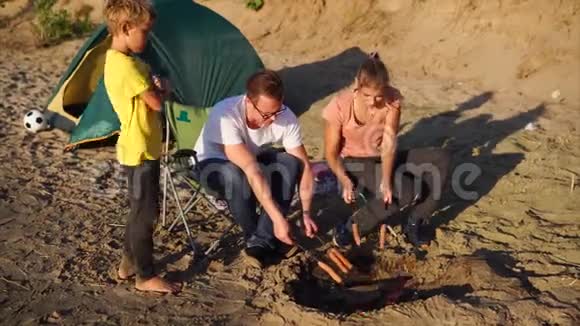 一个多风的夏日年轻的家庭在海滩上烤着香肠视频的预览图