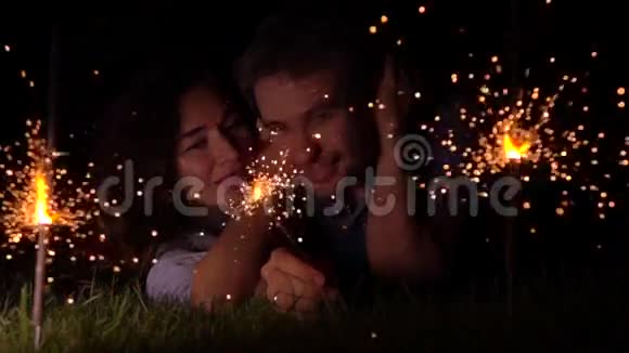 快乐可爱的女孩和男人躺在草地上晚上燃烧着火花超慢动作视频拍摄500视频的预览图