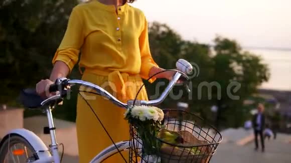 一个身穿黄色长裙的微笑着的黑发女人站在她的城市自行车旁车把手里拿着鲜花视频的预览图