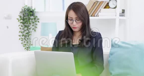 戴眼镜的年轻女性坐在沙发上在家里使用笔记本电脑在生活背景下工作室内视频的预览图