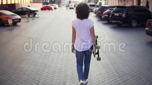一个女人早上拿着她的长板走在旧城街道上停在城市里美丽美丽视频的预览图