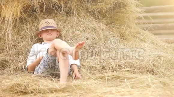 一个戴草帽的小男孩在干草堆里打盹从他的合唱团里休息一下视频的预览图