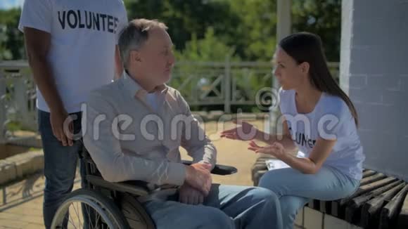 年轻的女志愿者和一个坐在轮椅上的男人交谈视频的预览图