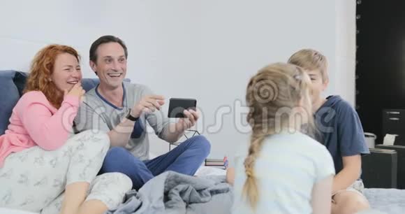 爆笑父母拍视频孩子坐在床上在卧室聊天幸福的家庭花时间视频的预览图