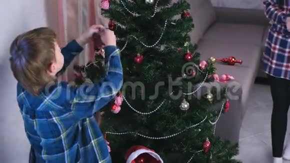 妈妈和儿子戴着圣诞帽用珠子和球装饰圣诞树视频的预览图