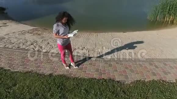 美丽的黑发卷发在河边读书视频的预览图