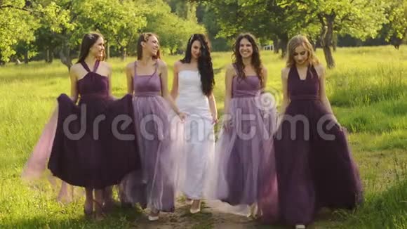 美丽的新娘和新娘穿着紫色的裙子晚上牵着手在公园或花园里散步大笑视频的预览图