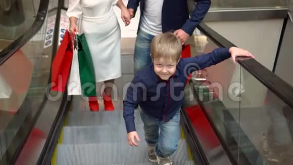 家庭圣诞购物带着孩子的父母带着礼物包上扶梯大型多色包装视频的预览图