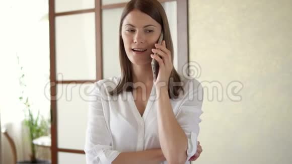 穿着白色衬衫的休闲年轻女子站在客厅里打电话收到坏消息视频的预览图