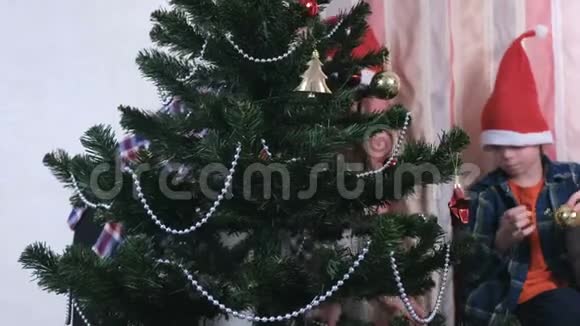 妈妈和儿子戴着圣诞帽用珠子和球装饰圣诞树视频的预览图