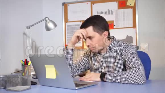 疲惫的网络管理员紧紧地抱住他的头在笔记本电脑上工作视频的预览图