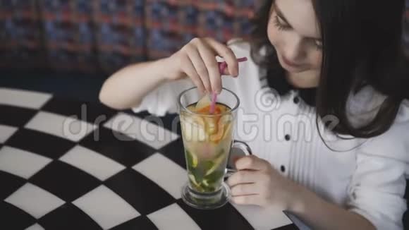 美丽的女孩在咖啡馆里用小管搅拌柠檬水对着镜头微笑视频的预览图