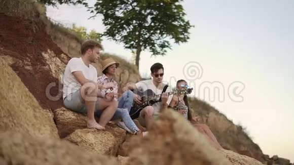 一群欢快的年轻人坐在海边的岩石上弹吉他唱歌跳舞视频的预览图