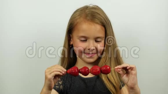 漂亮的女孩在串上品尝草莓微笑的女孩吃草莓舔嘴唇视频的预览图