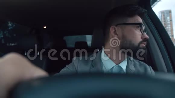 一个留着胡子和眼镜的年轻人在一辆好车的车轮后面视频的预览图