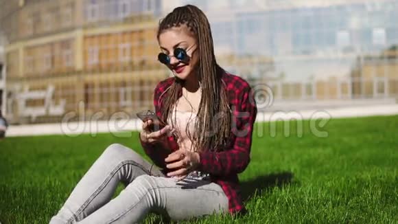 有恐惧的年轻女子在公园里放松坐在草地上听音乐戴墨镜的嬉皮士女孩视频的预览图