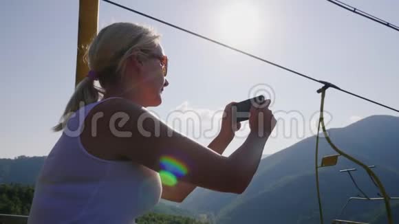 一个年轻的女人在夏天乘滑雪电梯他为美丽的风景拍照假期视频的预览图