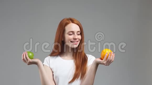 美丽的红头发女孩试图选择橙色或苹果健康食品选择理念视频的预览图