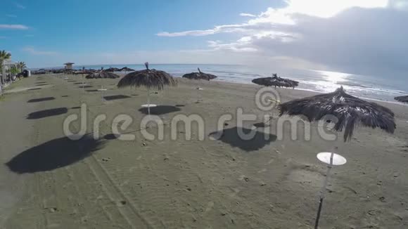 在稻草伞上方飞行的无人机在拉纳卡的海滩上观看放松视频的预览图