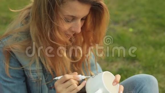 特写女性的手用白色杯子上的一根管子上的油漆画一个图案微笑的女孩在坐着画装饰品视频的预览图