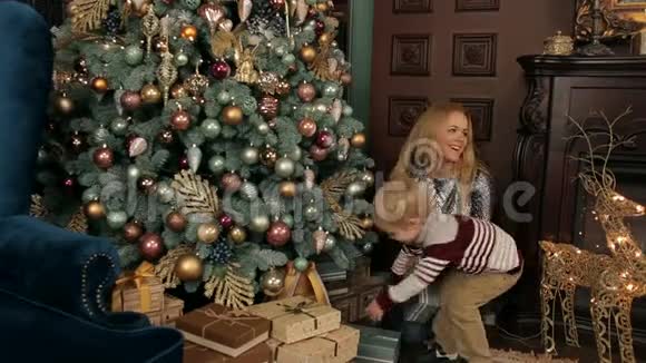 妈妈和儿子在圣诞树附近打开圣诞节视频的预览图