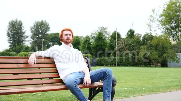 在公园坐在长凳上的人竖起大拇指红发和胡子视频的预览图