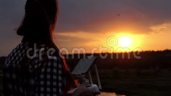 年轻女子在日落时分用一个面板来控制她的无人机视频的预览图
