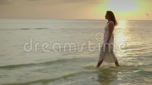一个穿着轻便夏装的年轻女子正在海的背景下沿着水边行走视频的预览图