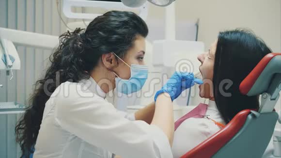年轻的医生是一个穿着医用白色衣服和口罩的女人做一个病人的回顾在考试期间视频的预览图
