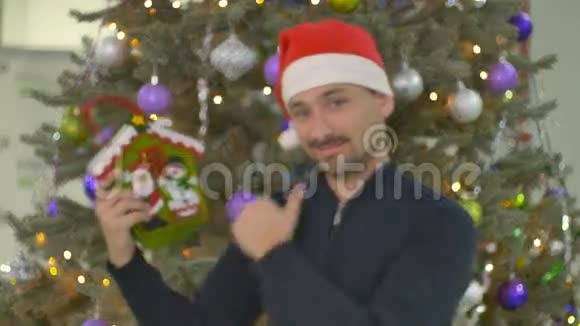有节日礼物的帅哥在圣诞树的背景上竖起大拇指视频的预览图