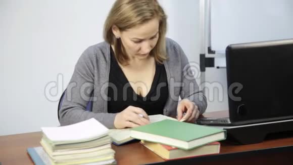 女学生在笔记本电脑前的一本书中阅读并做笔记视频的预览图