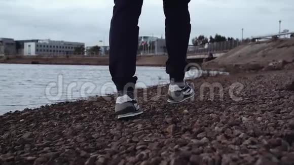 穿着时髦运动鞋的人的腿在城市的岩石海岸上行走视频的预览图