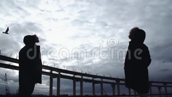 两个人的轮廓站在河岸与公路桥视频的预览图